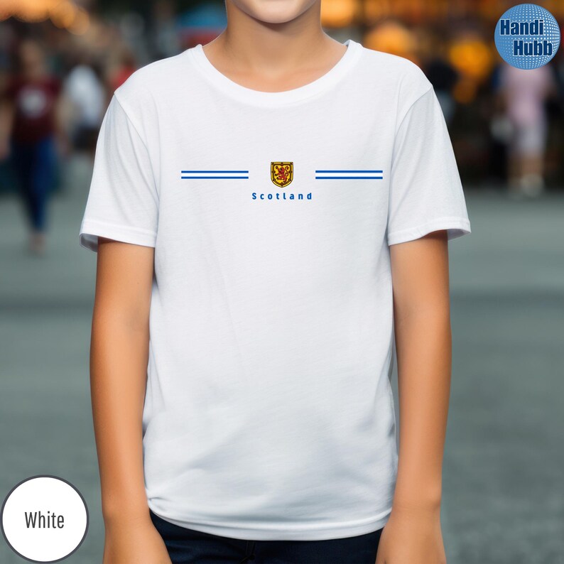 May include: White t-shirt with a blue stripe design and the word "Scotland" printed in blue. The shirt features a crest with a lion rampant. The shirt is a crew neck.