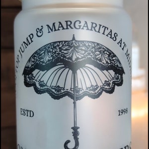 May include: White frosted glass jar with a bamboo lid and a black and white illustration of an umbrella with the text "Top Jump & Margaritas at Midnight" and "Owens Sisters Annual Parasol June" and "There's a Little Witch in All of Us" and "Maria's Island, Massachusetts".