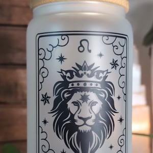 May include: A white glass water bottle with a bamboo lid and a black and white illustration of a lion with a crown and stars. The text "THE LEO FIRE ELEMENT / JUL. 23rd - AUG. 22nd" is printed on the bottle.