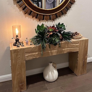 May include: A rustic wooden console table with a natural wood finish. The table has a single shelf and is decorated with a vase of succulents, a lamp, and figurines.