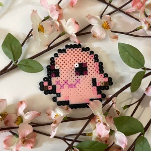 Könnte beinhalten: Rosa und schwarze Pixelkunst eines Comic-Charakters mit einem runden Kopf und einem kleinen Körper. Der Charakter ist von rosa Blumen umgeben.