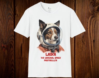 Könnte beinhalten: Weißes T-Shirt mit einem Hund, der einen Weltraumhelm und einen roten Raumanzug trägt. Der Text "LAIKA THE ORIGINAL SPACE PAWTRAILLER" ist rot unter dem Hund aufgedruckt.