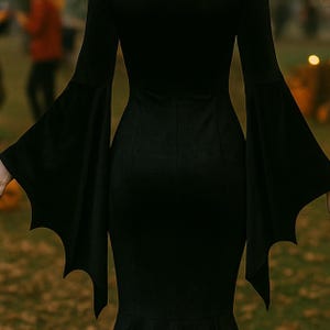May include: A black dress with batwing sleeves. The sleeves are long and flared, with a bat-wing shape at the ends. The dress has a fitted bodice and a flared skirt. The dress is made of a soft, flowing fabric.