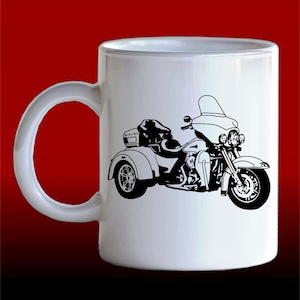 May include: White ceramic mug featuring a black silhouette of a three-wheeled motorcycle. The motorcycle has a windscreen, a sidecar, and a luggage rack.