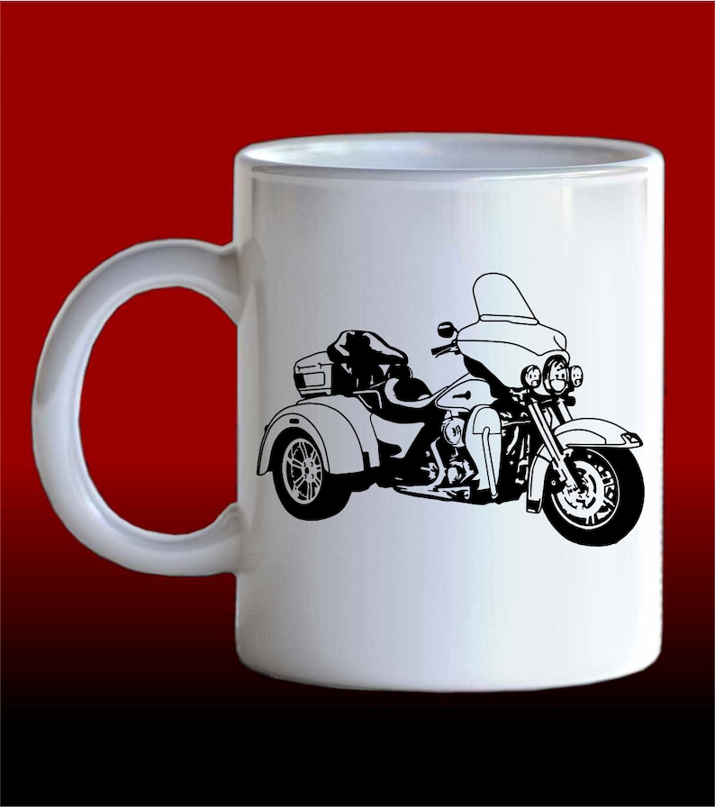 May include: White ceramic mug featuring a black silhouette of a three-wheeled motorcycle. The motorcycle has a windscreen, a sidecar, and a luggage rack.