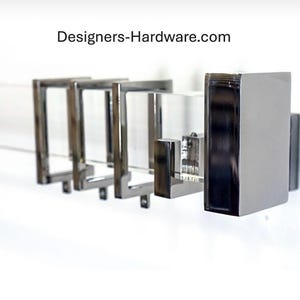 May include: A wall-mounted towel rack featuring a clear acrylic bar supported by four polished chrome square brackets. The text Designers-Hardware.com is visible above the hardware. The design includes a rectangular chrome end cap.