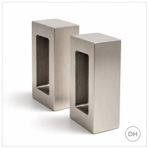 May include: Two rectangular, brushed silver metal flush pull handles standing upright. Each handle features a smooth, flat exterior surface and a deep, recessed rectangular opening in the center, showcasing a vertical grain texture within the cavity.