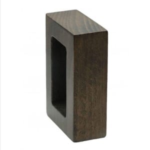 May include: A rectangular block made of dark brown wood with a smooth finish. The object features a large, hollow, rectangular opening in the center, creating a frame-like structure with thick, solid sides and a visible wood grain texture throughout.