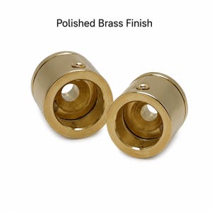 May include: Two cylindrical hardware components with a polished brass finish. Each piece features a hollow center with a recessed interior and a small circular screw hole on the outer side. The text "Polished Brass Finish" is visible above.