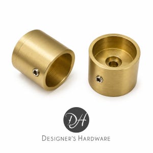 May include: Two cylindrical brass curtain rod brackets with a brushed finish. Each bracket features a hollow center, a circular base with a central hole for mounting, and a small silver-colored set screw on the side for securing a rod in place.