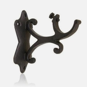 May include: A dark brown, cast metal curtain rod bracket featuring a vertical mounting plate with two screw holes and a curved, decorative support arm that extends outward to a U-shaped cradle designed to hold a rod, secured by a small metal screw.