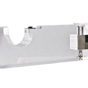 May include: A clear acrylic curtain rod bracket with a silver metal mounting plate. The bracket has a round opening for the curtain rod to pass through.