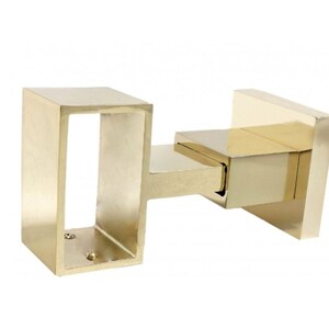 May include: A gold-colored, rectangular curtain rod bracket. The bracket has a square base, a rectangular arm, and a rectangular opening for the curtain rod. The bracket is made of metal and has a shiny finish.