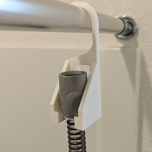 May include: White 3D printed holder for a gray CPAP hose with a ResMed logo. The holder is attached to a silver shower rod.