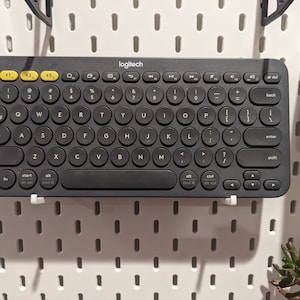May include: A black Logitech keyboard with round keys and a white background. The keyboard has a number pad, function keys, and arrow keys. The text "logitech" is printed in white on the top of the keyboard.