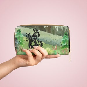 May include: A green and brown zippered wallet with a watercolor design of a woman riding a horse through a forest.