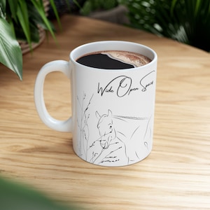 May include: White ceramic mug with a black line drawing of a horse in a field. The mug has the text "Wide Open Space" written on it.