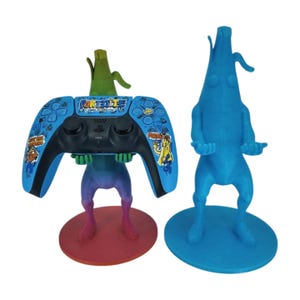 May include: Two 3D printed Fortnite character controller stands. One is blue and shaped like a banana, the other is a multi-colored character holding a blue and white PlayStation 5 controller with Fortnite branding.
