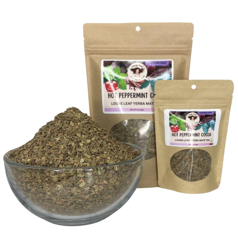 Peut inclure: Un bol en verre transparent rempli de feuilles de th&eacute; en vrac est plac&eacute; devant deux sachets de th&eacute; en papier brun. Les sachets portent les inscriptions "Hot Peppermint Cocoa" et "Hot Peppermint Chai". Les feuilles de th&eacute; sont vertes et brunes.