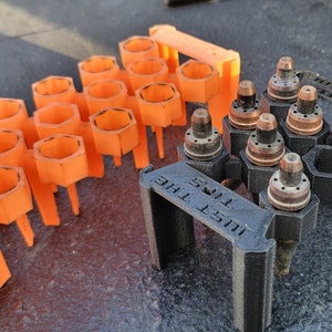May include: Two 3D printed organizers for small tools. The orange organizer has 16 hexagonal slots. The black organizer has 7 hexagonal slots and the text "JUST THE TIPS" on the front.