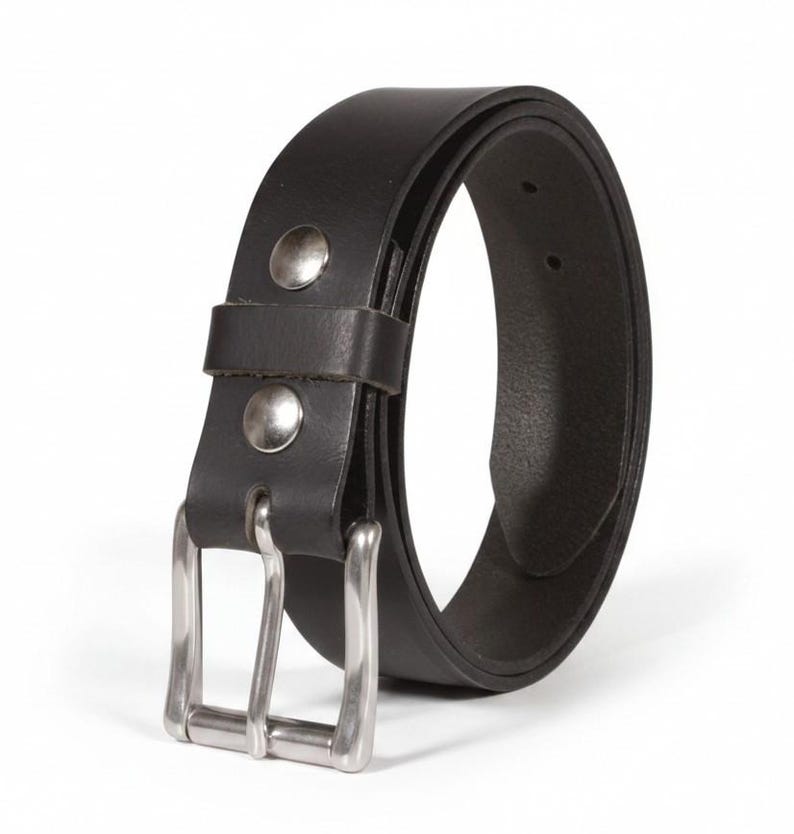 May include: A black leather belt with a silver-colored buckle and two silver rivets. The belt is curved, showing its thickness and the details of the buckle design. The belt is a classic accessory.