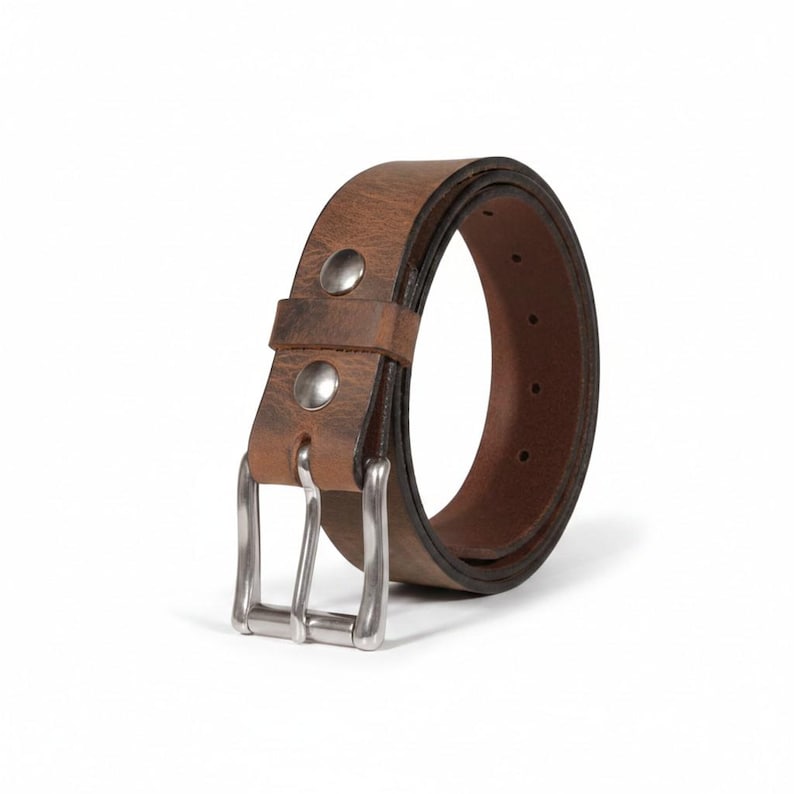 May include: A brown leather belt with a silver-colored buckle. The belt has two silver rivets near the buckle. The leather has a distressed appearance. The belt is approximately 1.5 inches wide.