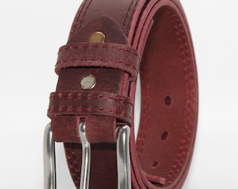 May include: A dark burgundy leather belt featuring a smooth texture, double-stitched edges, and a rectangular silver-toned metal buckle. The belt includes a matching leather keeper loop secured by two small metallic rivets near the buckle assembly.