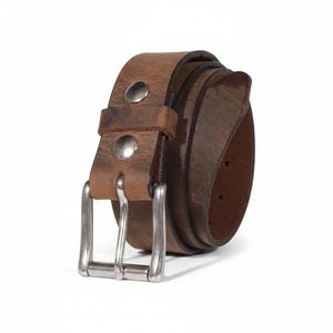 May include: A rolled-up brown leather belt with a silver-colored buckle and two silver rivets. The belt has a distressed appearance, suggesting a vintage or worn look. The background is plain white.