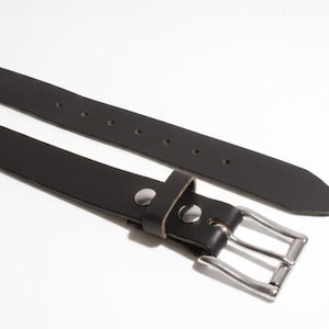 May include: A black leather belt with a silver-colored buckle and a matching silver-colored rivet. The belt is shown against a white background. The belt has a width of approximately 1.25 inches.
