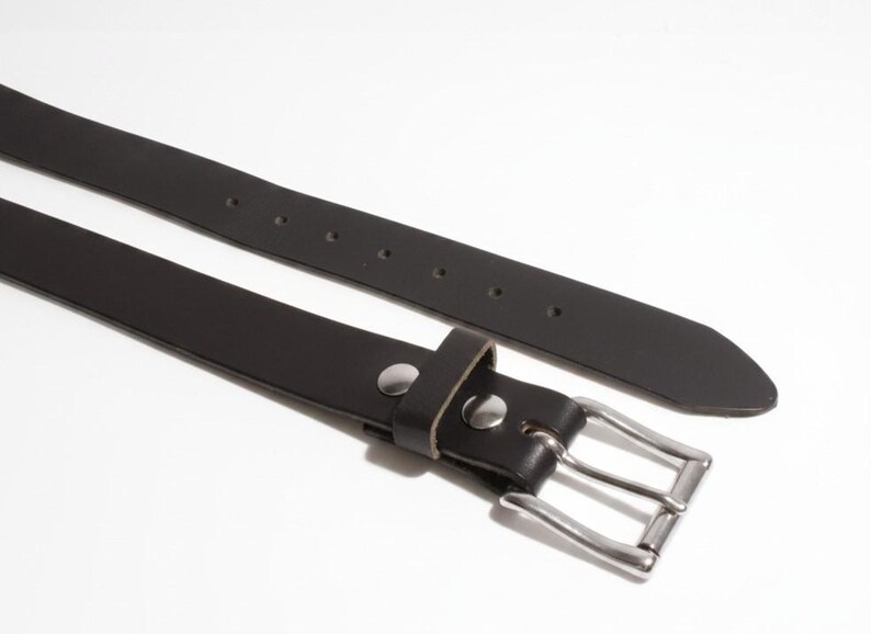 May include: A black leather belt with a silver-colored buckle and a matching silver-colored rivet. The belt is shown against a white background. The belt has a width of approximately 1.25 inches.