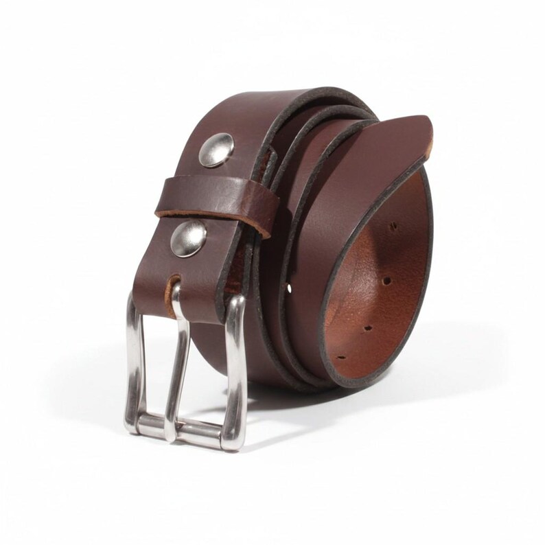 May include: A rolled-up brown leather belt with a silver-colored buckle and two silver rivets. The belt is made of a smooth, dark brown leather and is designed for everyday wear.