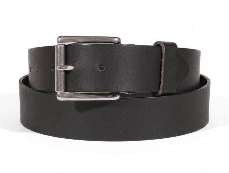 May include: A black leather belt with a silver-colored rectangular buckle. The belt is rolled up, showing the full width and thickness of the leather. The buckle is a simple, classic design.
