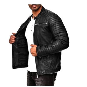 May include: Black leather jacket with quilted shoulder and sleeve detailing. The jacket features a zip closure, multiple pockets, and a stand-up collar. The model is wearing a white shirt underneath.