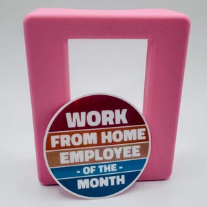 May include: A round sticker with a red, orange, blue, and white striped background. The sticker says "Work From Home Employee - Of The - Month".