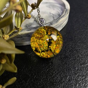 May include: A silver chain necklace with a round pendant featuring a yellow and green pressed flower design encased in clear resin.