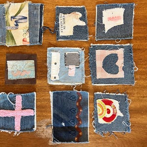 Könnte beinhalten: Neun Jeansstoffquadrate mit verschiedenen Designs. Einige Quadrate zeigen Stoffe mit floralen Mustern, Text oder abstrakten Formen in Rosa, Rot und Weiß. Die Quadrate sind auf einer Holzoberfläche angeordnet.