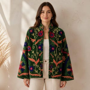 May include: A dark green velvet jacket featuring an open front and a mandarin collar. The garment is decorated with vibrant floral embroidery in shades of red, orange, and blue, with long, wide sleeves and a straight hemline over a white top.