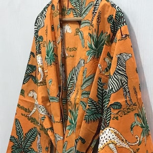 May include: An orange robe with a jungle-themed print featuring zebras, leopards, and lush green foliage. The robe is made of a lightweight fabric and has a tie closure at the waist. The robe is hanging on a wooden hanger.