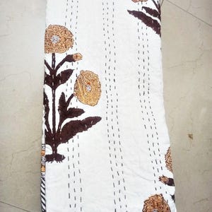May include: White quilt with a floral design. The quilt features brown and tan flowers with dark brown stems and leaves. The quilt is stitched with vertical lines of black thread.