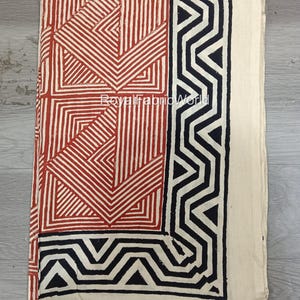 May include: A folded fabric with a geometric pattern in red and black on an off-white background. The design includes angular lines and shapes, with the text "Royal Fabric World" visible. The fabric is likely for crafting or home decor.