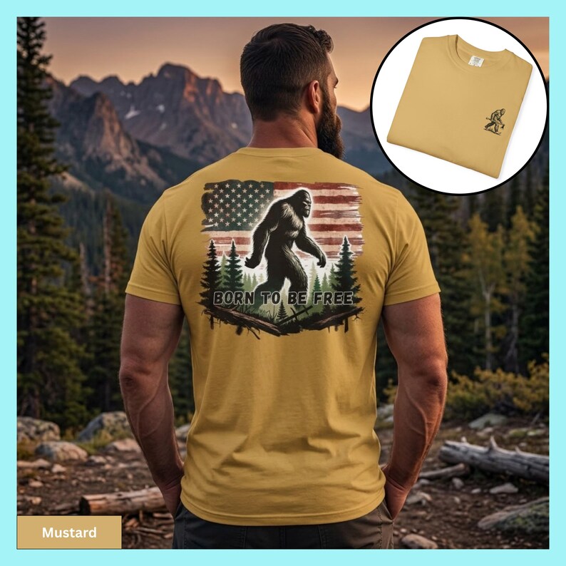May include: Mustard-colored t-shirt featuring a Bigfoot graphic with an American flag design and the text "BORN TO BE FREE." The shirt is displayed on a person with a mountain backdrop. A smaller image shows the shirt folded.