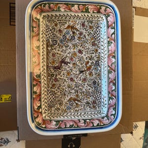 May include: A rectangular ceramic serving tray featuring a white base with a detailed hand-painted pattern of colorful flowers, foliage, and birds. The border is decorated with a repeating pink and green leaf motif and a thin blue rim.
