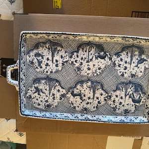 May include: A rectangular ceramic serving tray featuring a white base with a dark blue intricate pattern. The design consists of six quatrefoil-shaped panels containing illustrations of animals and trees, set against a cross-hatched background.