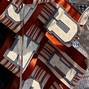 May include: A red, white, and blue ribbon with the letters "J, M, D, R" in white with black polka dots. The ribbon is decorated with a blue flower.