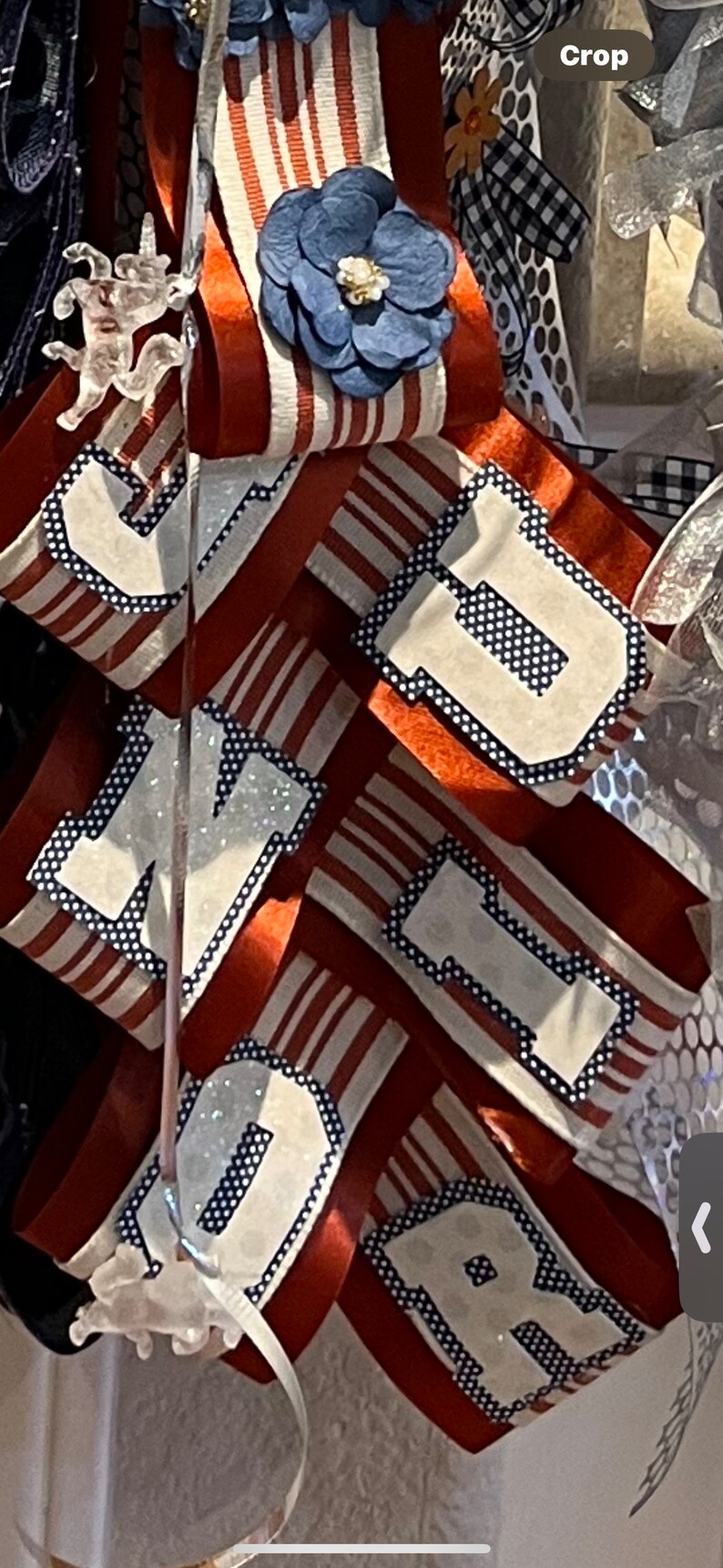 May include: A red, white, and blue ribbon with the letters "J, M, D, R" in white with black polka dots. The ribbon is decorated with a blue flower.