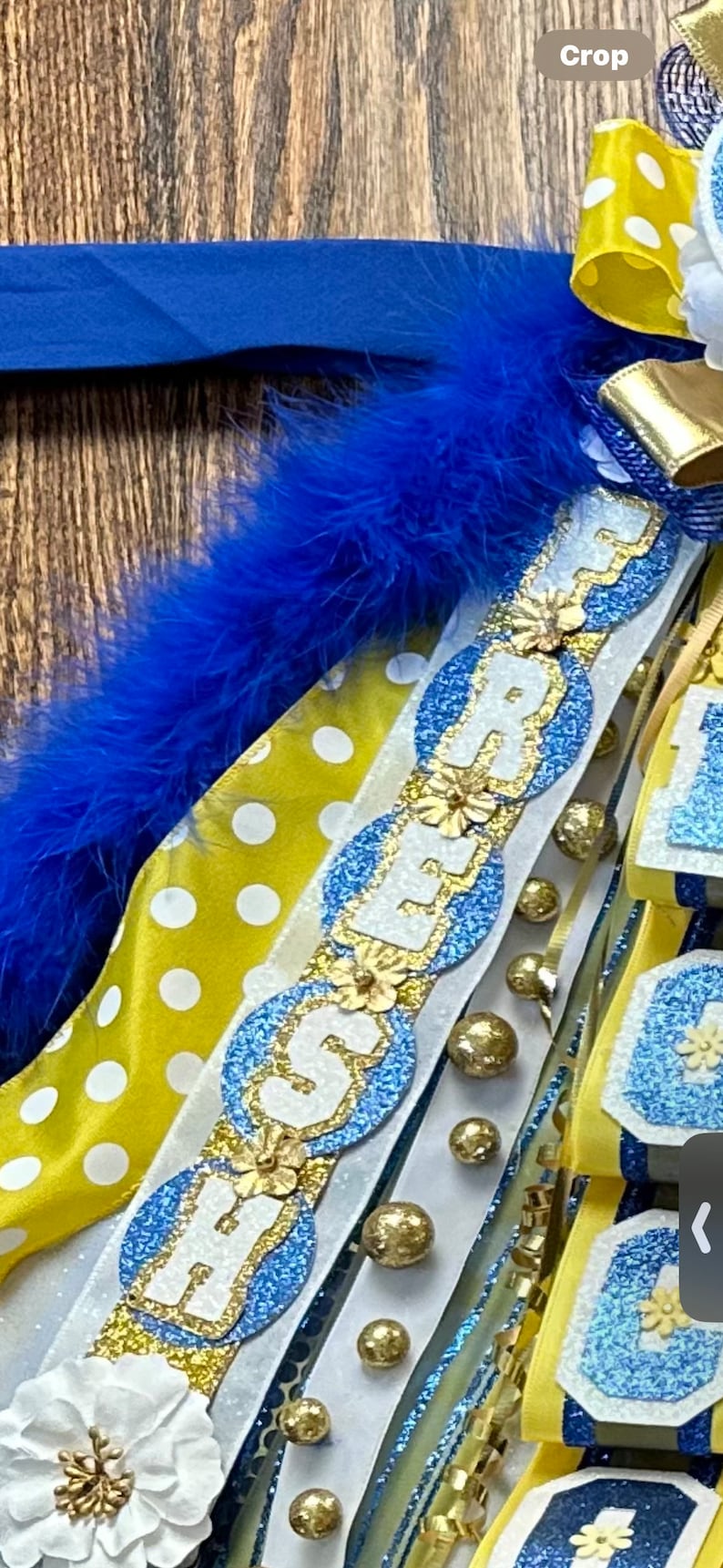 May include: A blue and gold graduation sash with the word "FRESHMAN" spelled out in white letters with gold trim. The sash is decorated with white flowers, gold beads, and blue and white polka dot ribbon.