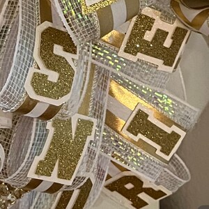 May include: Gold glitter letters spelling "Senior" on a white and gold ribbon with a chevron pattern.