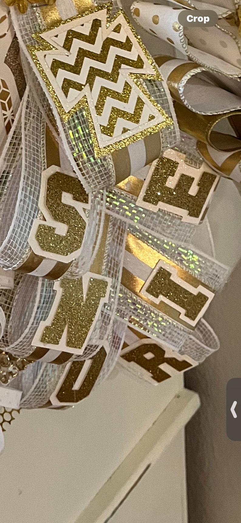 May include: Gold glitter letters spelling "Senior" on a white and gold ribbon with a chevron pattern.