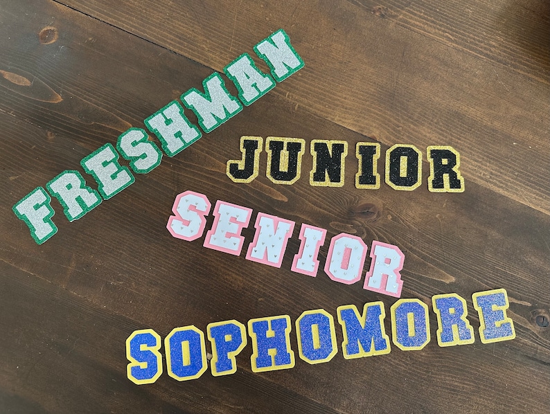 May include: Five glitter iron-on patches with the words "Freshman", "Junior", "Senior", "Sophomore" in different colors.