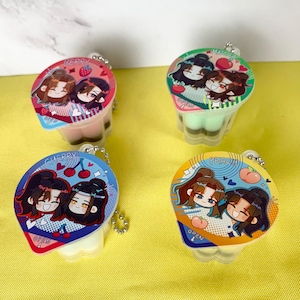 May include: Four colorful keychains featuring cartoon illustrations on the lids. Each keychain has a different fruit theme: berry, cherry, matcha, and peach. The lids have the word "OPEN" printed on them.